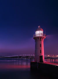 Illuminated lighthouse by sea against sky at night