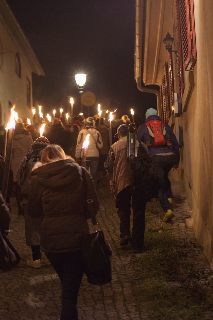 REAR VIEW OF PEOPLE WALKING ON ILLUMINATED STREET IN CITY