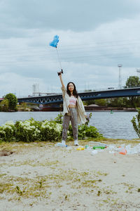 Full length portrait of confident young woman picking garbage near river