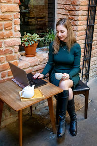 Woman holding coffee cup while using laptop on table at sidewalk cafe