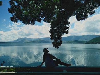 Man sitting by lake against sky