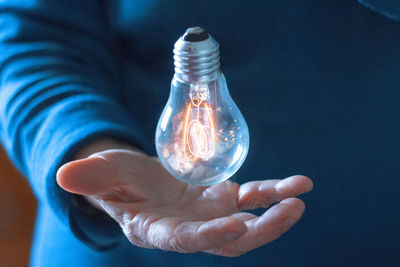 Close-up of illuminated light bulb levitating on hand