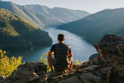 Rear view of man sitting on rock by mountains