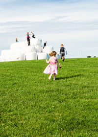 Children by covered hay bales on grassy field against sky