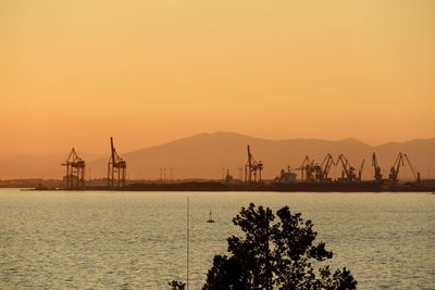 Cranes at commercial dock against sky during sunset