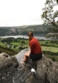 Side view of woman sitting on rock against sky