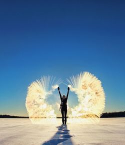 Rear view of woman throwing powder snow while standing on landscape against clear blue sky