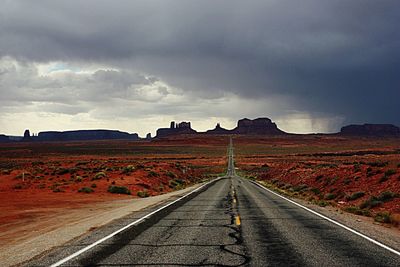 Road passing through field against cloudy sky