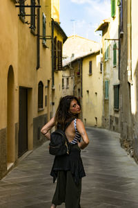 Portrait of woman with backpack walking amidst buildings