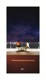 Rear view of people sitting on beach against sky