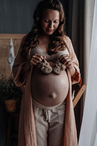 Pregnant woman with mug of hot herbal tea staying in front of window. expecting new baby