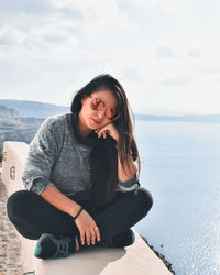 Young woman sitting on sea shore against sky