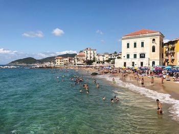 People on sea by city against sky