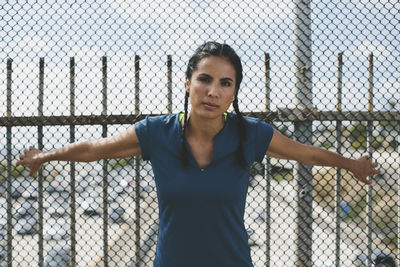 Portrait of confident athlete standing against chainlink fence