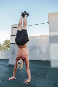 Full length of shirtless man exercising against sky