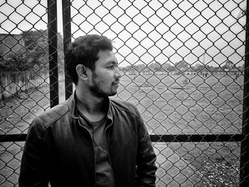 Portrait of young man looking through chainlink fence