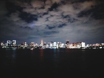 Illuminated buildings by river against sky in city at night