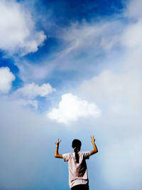 Rear view of man with arms outstretched standing against sky