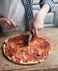 The hand holds a round knife and cuts a pizza with salami, close-up. 