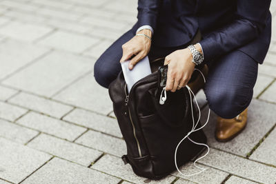 Low section of male entrepreneur putting paper in bag while crouching on street