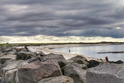 People on rocks by sea against sky