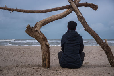 Rear view of woman sitting amidst tree trunk at beach