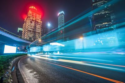 Light trails on road amidst illuminated buildings in city at night