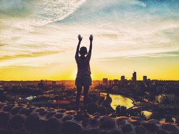 Silhouette of woman standing against cityscape at sunset