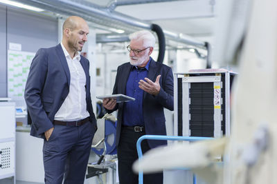 Senior male manager discussing over digital tablet with colleague while standing by machinery at factory