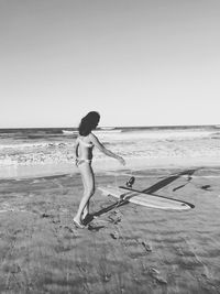 View of woman with surfboard on beach against clear sky