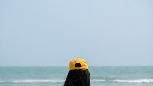 The woman's head is wearing a yellow hat staring at the sea.