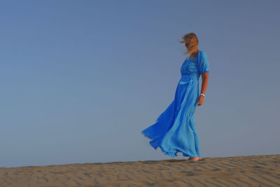 Woman wearing blue dress while standing in desert against blue sky