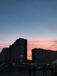 People on street by buildings against sky at sunset