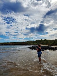 Man fishing at beach against sky