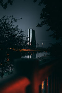 Silhouette factory by lake against sky at night