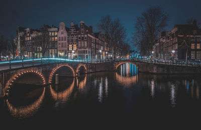 Illuminated bridge over river in city against sky at night