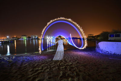 Blurred motion of woman on illuminated land against sky at night