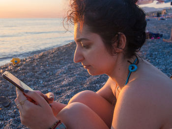 Side view of young woman using mobile phone at beach