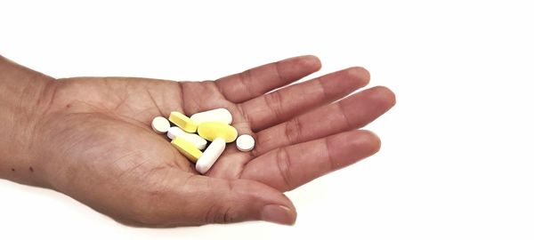 Cropped hand of person holding pills against white background