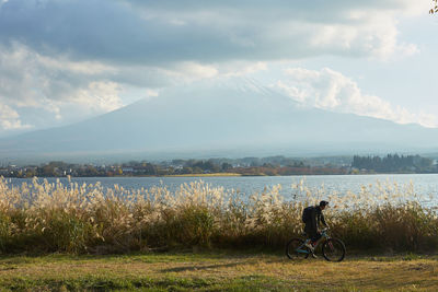 Scenic view of man cycling by lake and mountains against sky