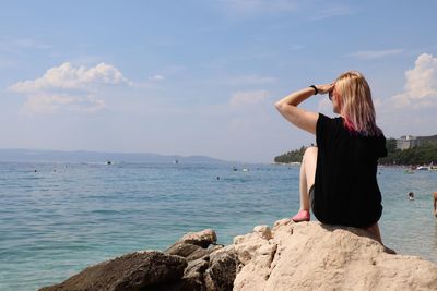 Rear view of woman sitting on rock at beach