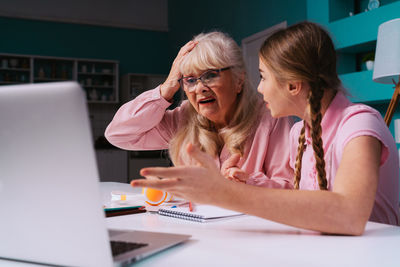 Surprised grandmother and granddaughter gesturing while looking at laptop