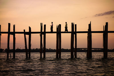 Silhouette wooden posts in sea against sky during sunset