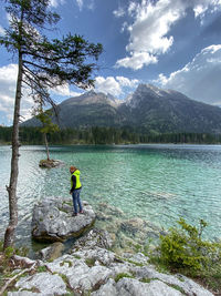 Woman stands by a lake in front of a mountain range