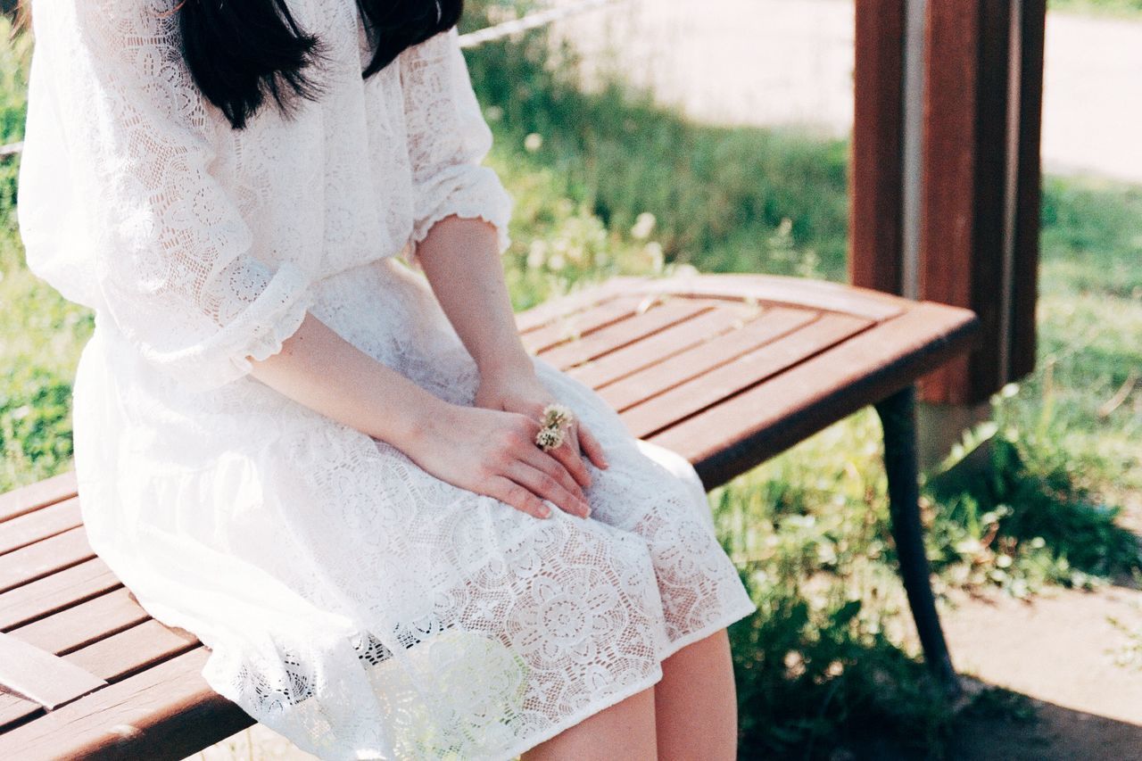 MIDSECTION OF WOMAN SITTING ON BENCH AT PARK