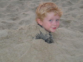 Portrait of playful boy covered with sand at beach