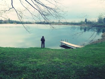 Rear view of man standing at lakeshore against sky