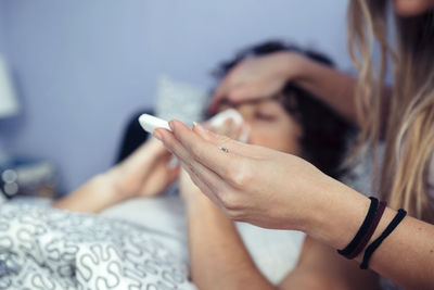 Close-up of woman measuring temperature with thermometer of friend