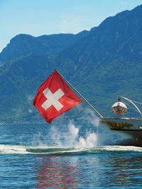 Swiss flag on boat in lake against mountains
