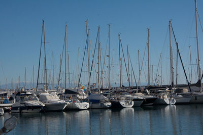 Sailboats moored in harbor against clear blue sky